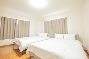 Habitación de hotel con dos camas individuales, cortinas color beige y suelo de madera.