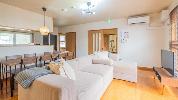 A modern living room with a sofa, a dining area with wooden tables and chairs, a TV, and a ceiling fan. - UNO Toyako (Toyako)