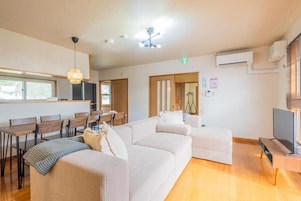 Una sala de estar moderna con un sofá, un comedor con mesas y sillas de madera, un televisor y un ventilador de techo.