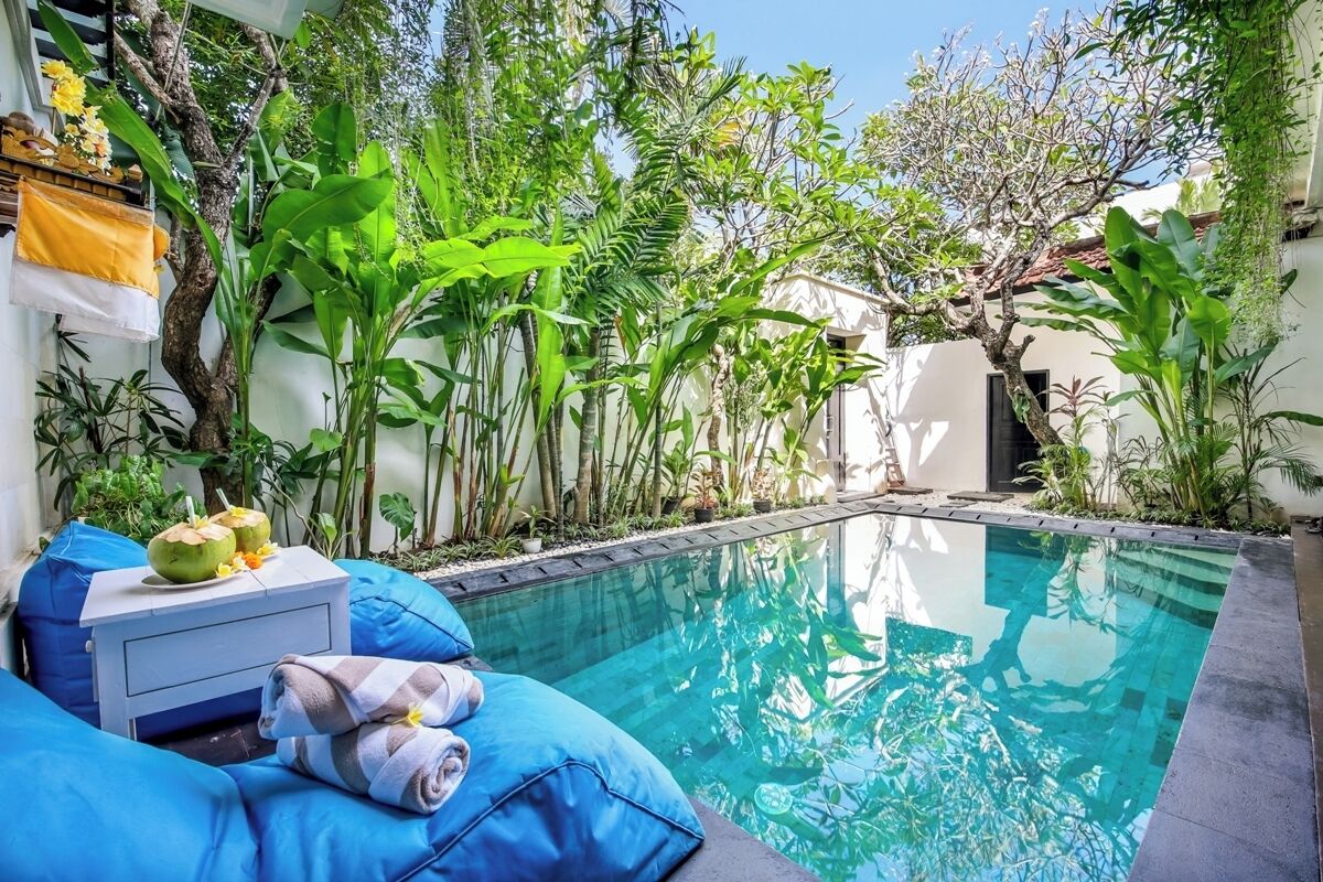 A poolside area with a clear pool, blue cushions, and tropical plants.