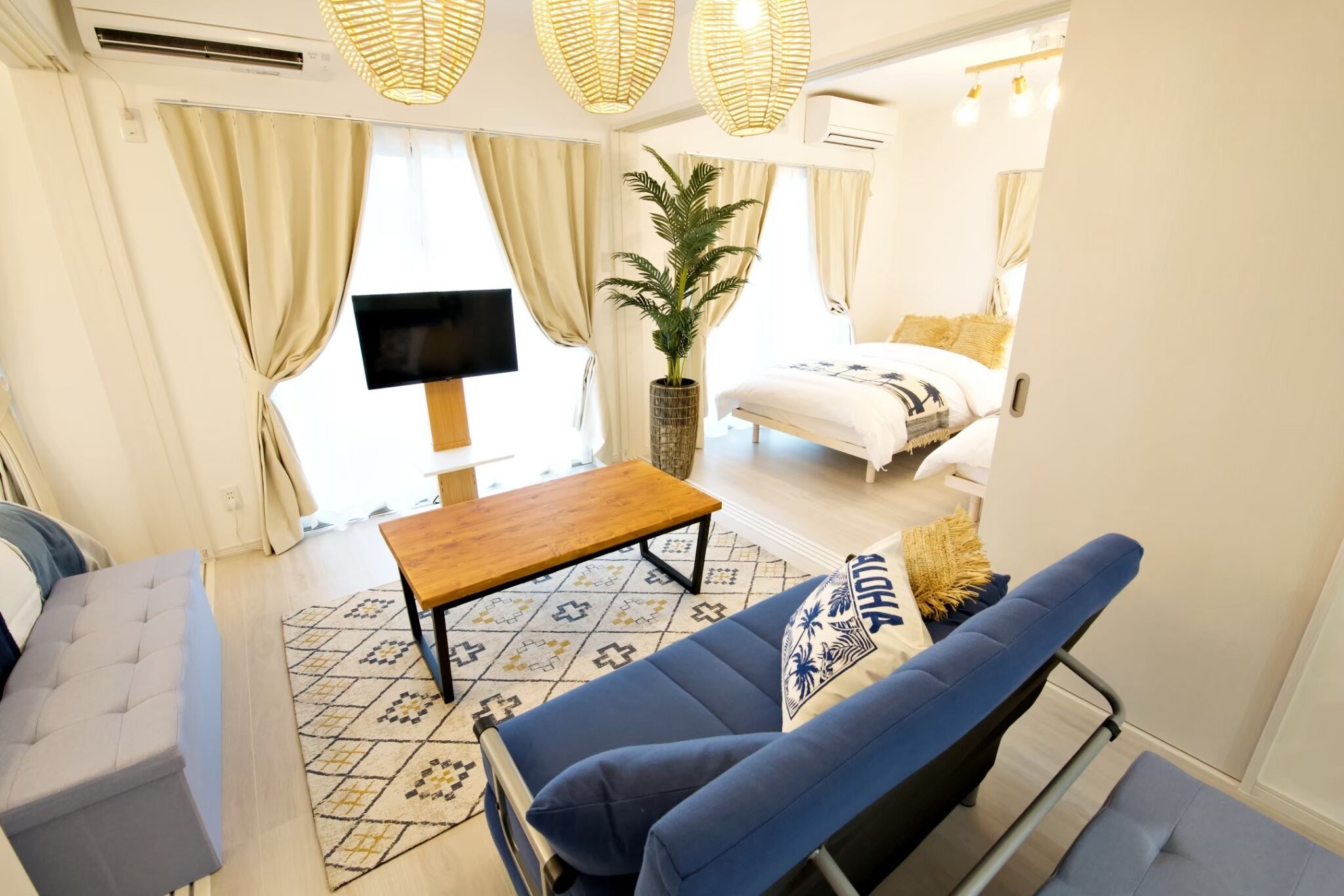 A modern living room with a sofa, a coffee table, a TV, and a bed with a white duvet.