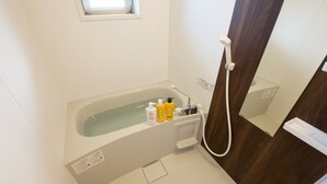 A modern bathroom with a bathtub, a handheld showerhead, and toiletries. - Ocean Terrace SESOKO 203 (Motobu)