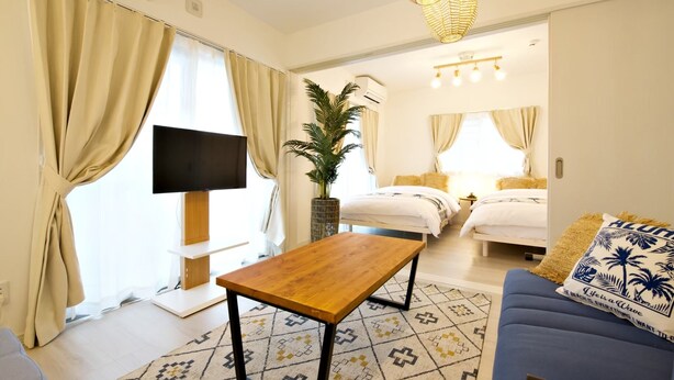 A hotel room with a TV, a wooden table, a sofa, a bed, and a potted plant. - Ocean Terrace SESOKO 203 (Motobu)