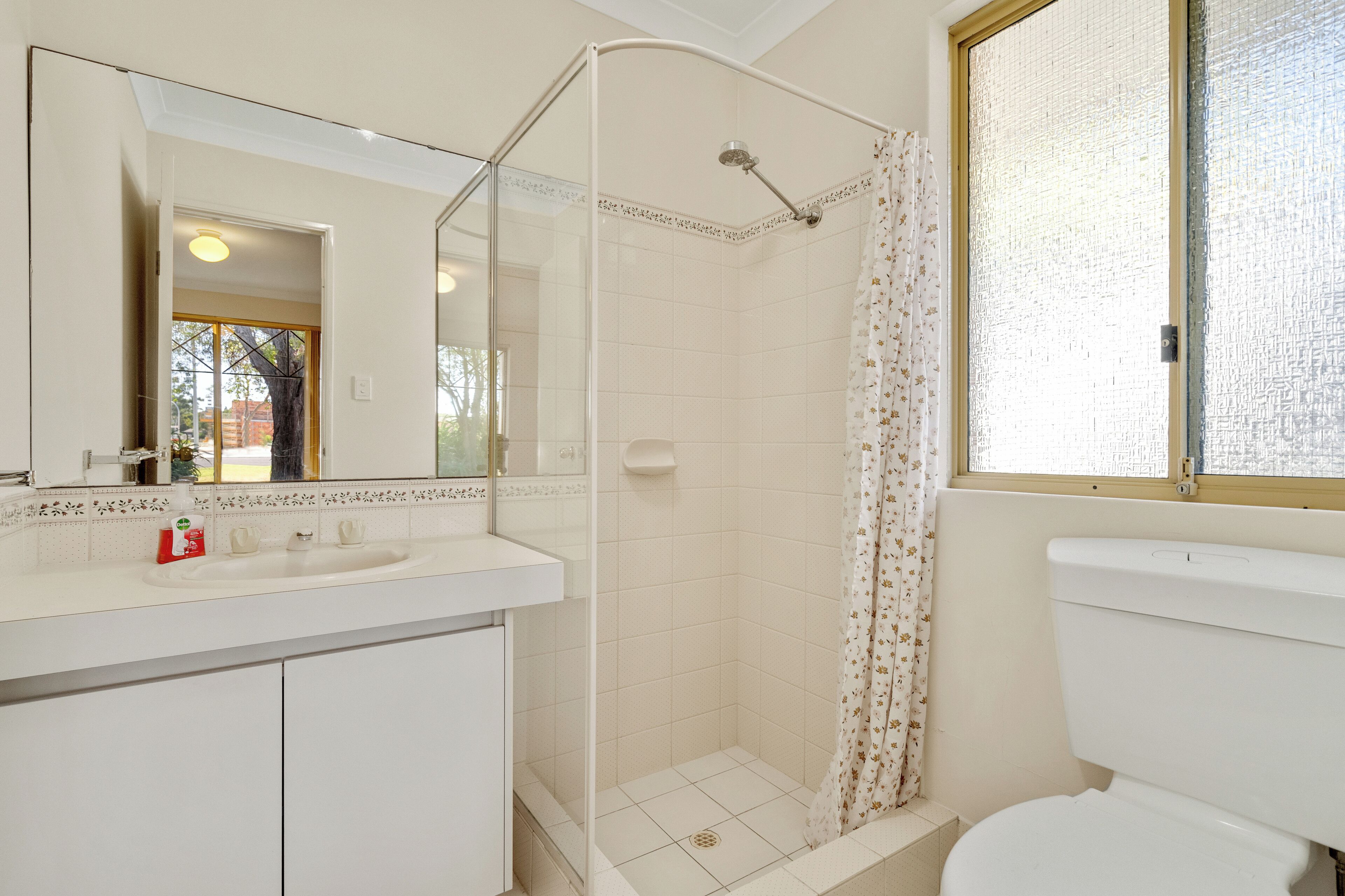 A bathroom with a shower, toilet, sink, and a large mirror.