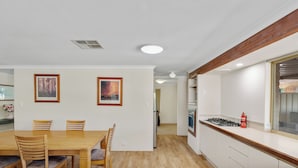 Een moderne keuken met witte kastjes, een houten aanrecht en een gasfornuis. Er is een zithoek met een houten tafel en stoelen.