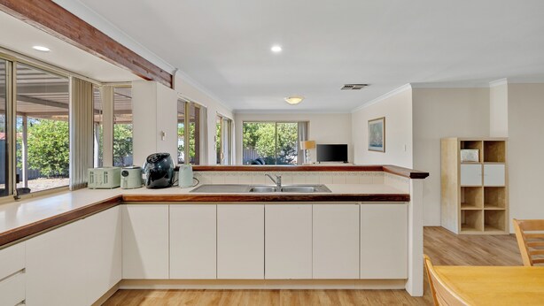 Een moderne keuken met witte kasten, een houten aanrechtblad en een groot raam met uitzicht op groen.