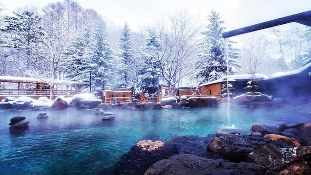 Une station de sports d’hiver dotée d’une source d’eau chaude, entourée d’arbres couverts de neige et de bâtiments en bois.