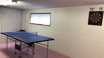 A ping pong table in a room with a dartboard on the wall.