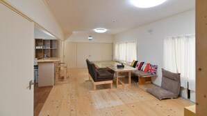 Un vaste espace de vie doté d’un plancher en bois, d’un ensemble de canapés, d’une table à manger et d’un coin cuisine à l’arrière-plan.