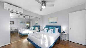 A bedroom with a large bed, a ceiling fan, a desk, and a mirror. - Coastal unit at sunset cliffs San Diego (San Diego)