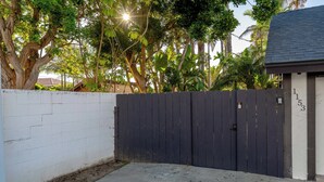 A gated area with a white brick wall, a dark wooden fence, and a house with a dark roof. - Coastal unit at sunset cliffs San Diego (San Diego)