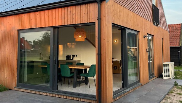 Une maison moderne avec un toit en pente, de grandes fenêtres en verre et une façade en bois.