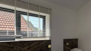 A bedroom with two beds, a wooden headboard, and a window with blinds.