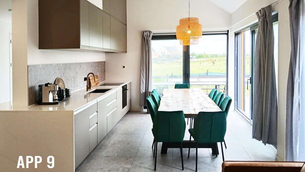 Een moderne keuken met een groot kookeiland, een eethoek met groene stoelen en uitzicht op de omgeving.