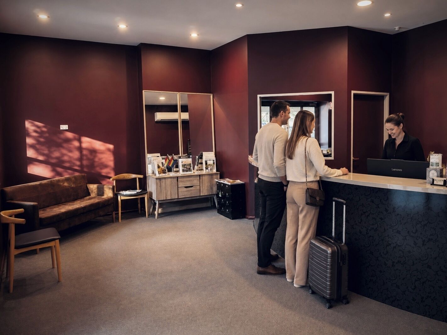 A reception area with a reception desk, a sofa, a chair, and a large mirror.