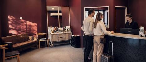 A reception area with a reception desk, a sofa, a chair, and a large mirror.