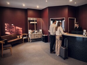 A reception area with a reception desk, a sofa, a chair, and a large mirror. - Reisen Hotel Hahndorf (Hahndorf)