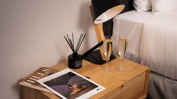 A neatly arranged bedside table with a magazine, a lamp, and two glasses of champagne.