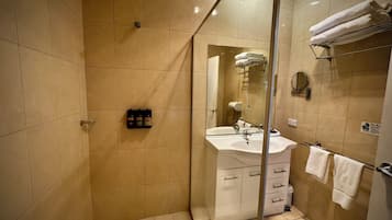 Un baño moderno con cabina de ducha de vidrio, un lavamanos blanco con espejo y un perchero para toallas.