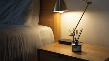 A neatly made bed with white linens, a wooden nightstand with a lamp and a container of reed diffusers, and a wooden headboard.