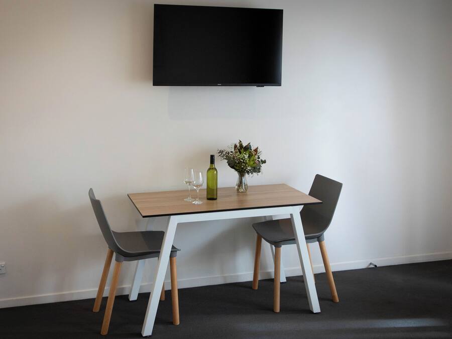A dining area with a table, two chairs, a bottle, and a vase of flowers.