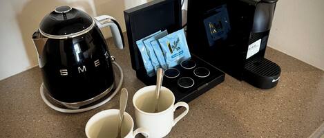 A coffee maker, two white mugs, and a packet of coffee pods on a kitchen counter.