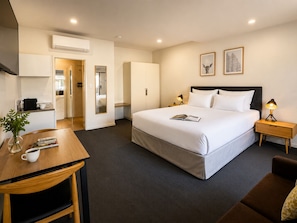 Habitación de hotel con cama, mesitas de noche, escritorio, silla, taza de café y una planta.