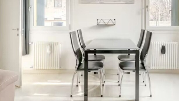 Un comedor moderno con una mesa y sillas, ventanas amplias, un radiador y un mapa mundial en la pared.