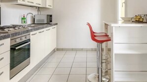 Una cocina moderna con armarios blancos, estufa a gas, horno y un taburete rojo.