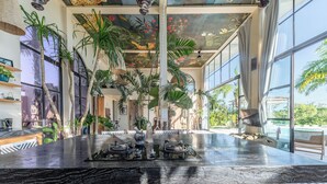 A spacious indoor area with a large, polished marble counter, multiple potted plants, and large windows offering views of the outdoors. - The Castle (Pecatu)