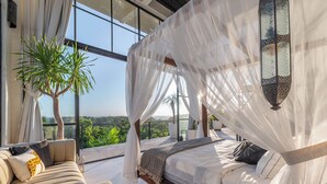 A bedroom with a canopy bed, a sofa, and a large window offering a view of greenery. - The Castle (Pecatu)