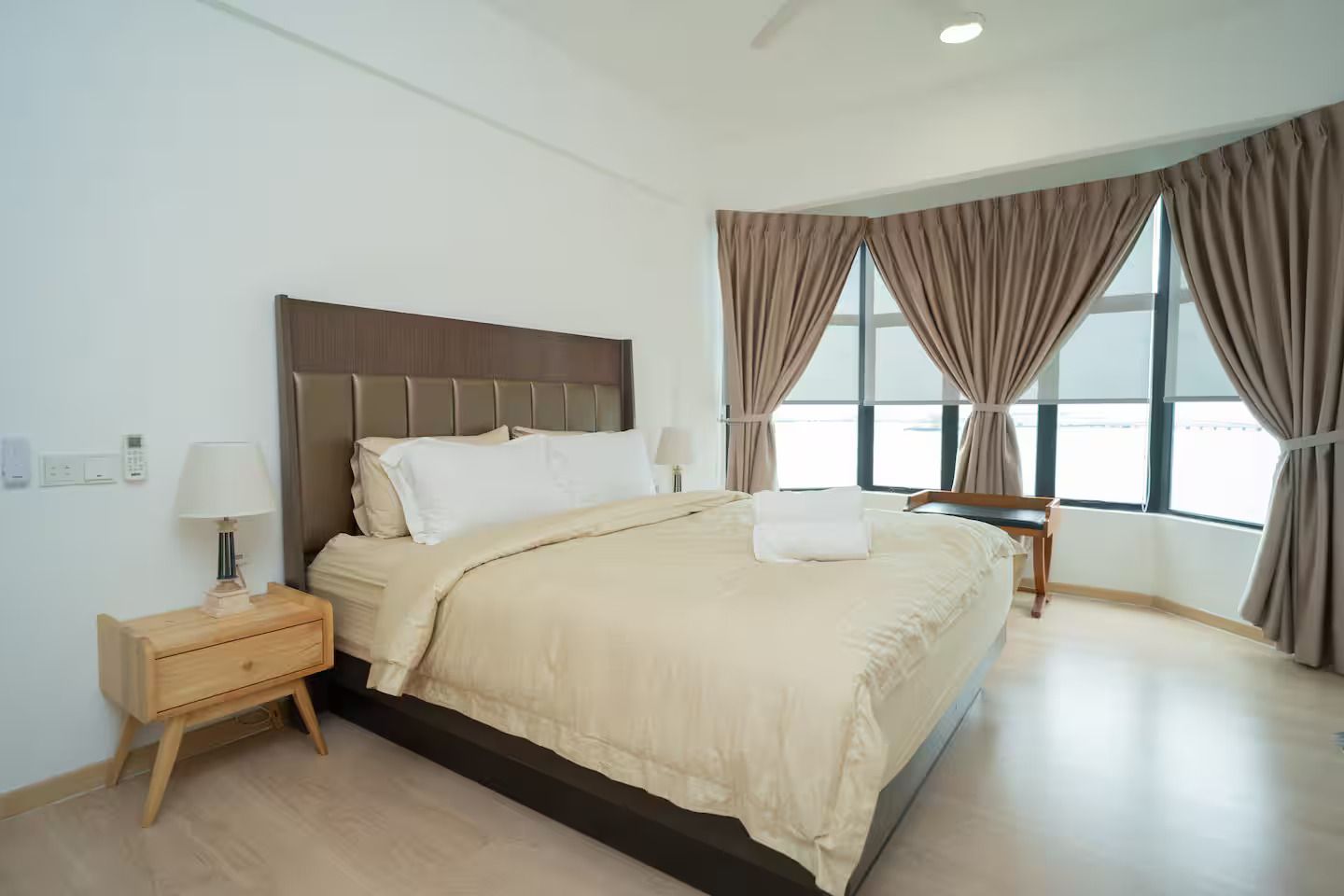 Ein Hotelzimmer mit Bett, Nachttisch, Lampe und Blick ins Freie durch große Fenster.