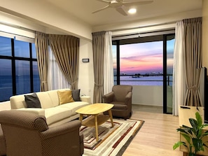Un salon moderne avec un canapé, un fauteuil et une table basse, de grandes fenêtres avec des rideaux et une vue sur la mer.