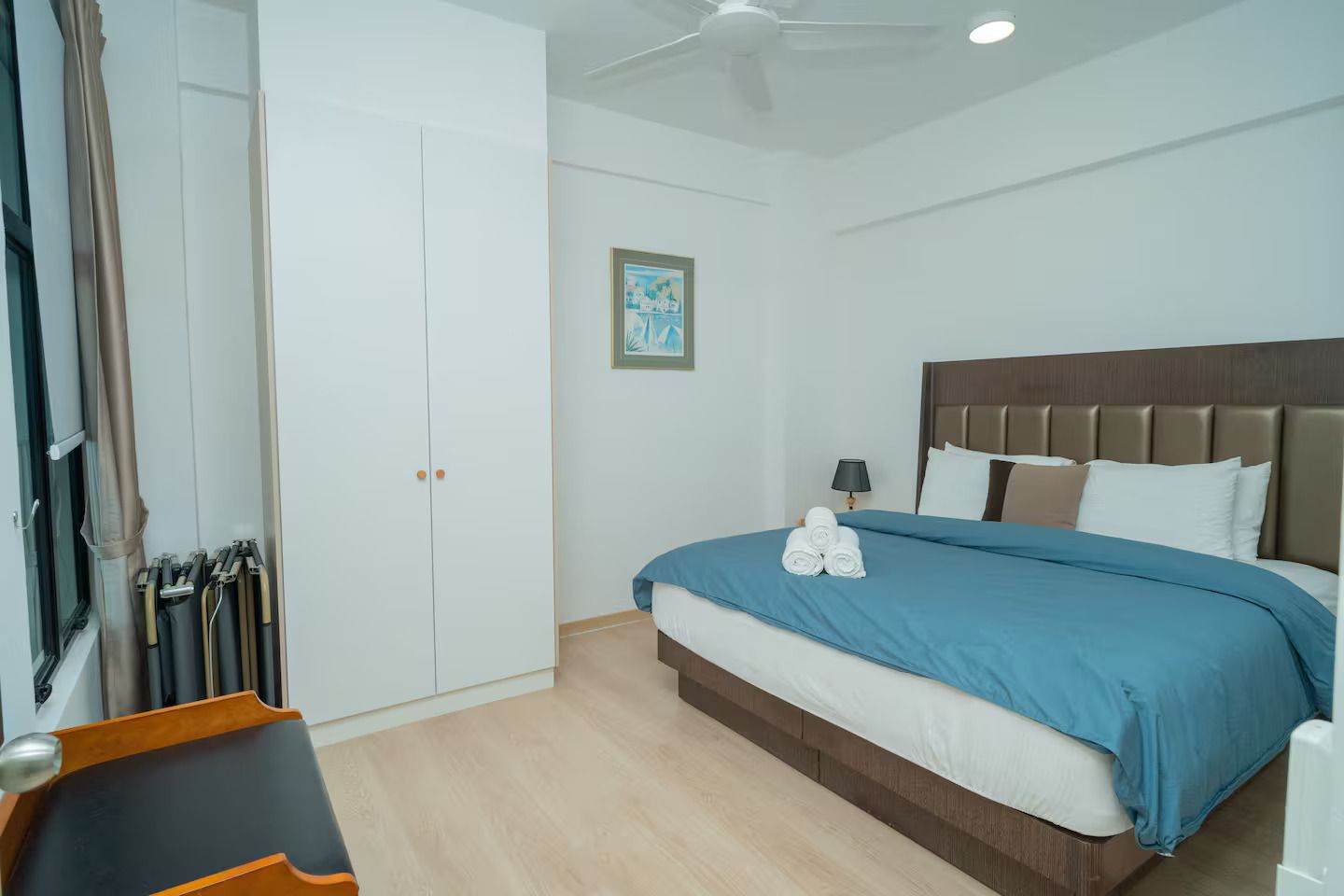 Ein Hotelzimmer mit Bett, Kleiderschrank, Deckenventilator und einem gerahmten Bild an der Wand.