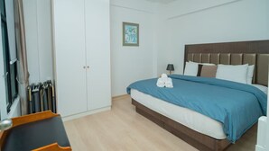Quarto de hotel com uma cama, um guarda-roupa, um ventilador de teto e uma moldura com um quadro na parede.