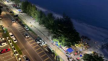 Eine Küstenstraße mit parkenden Autos und einer Strandpromenade, an der sich Menschen und Zelte befinden.
