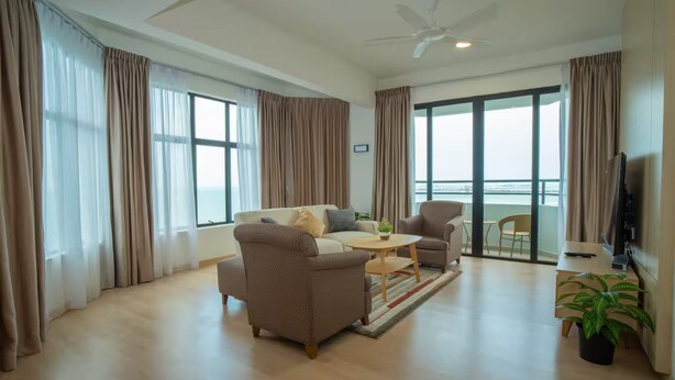 Uma sala de estar moderna com sofá, poltrona, mesa de centro e televisão. Há uma varanda com vista.
