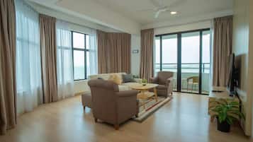 Ein modernes Wohnzimmer mit Sofa, Sessel, Couchtisch und Fernseher. Ein Balkon bietet einen Ausblick.
