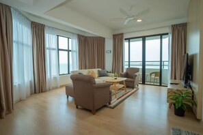 Una sala de estar moderna con sofá, sillón, mesa de centro y televisor. Hay un balcón con vistas.