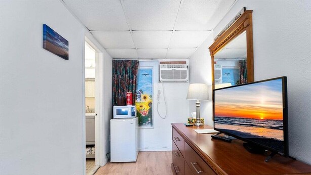 Une chambre de taille modeste, équipée d’une commode en bois, d’un téléviseur à écran plat, d’un four à micro-ondes et d’un petit réfrigérateur.