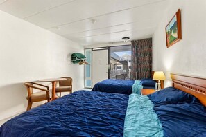 Een hotelkamer met twee bedden, een kleine tafel met stoelen, een balkon met uitzicht en een deur naar buiten.