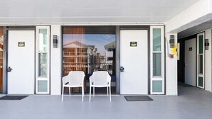 L’entrée d’un hôtel, avec deux chaises blanches à l’extérieur, des portes numérotées 109 et 108, et une vue sur la rue à travers les portes vitrées.