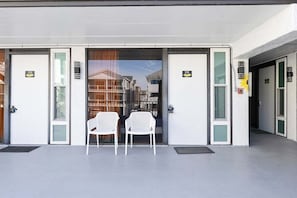 A hotel entrance with two white chairs outside, doors numbered 109 and 108, and a view of a street through the glass doors.