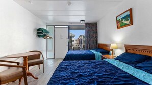 Une chambre d’hôtel avec deux lits, une chaise, une table, un tableau et une vue sur les bâtiments, visible à travers une porte.