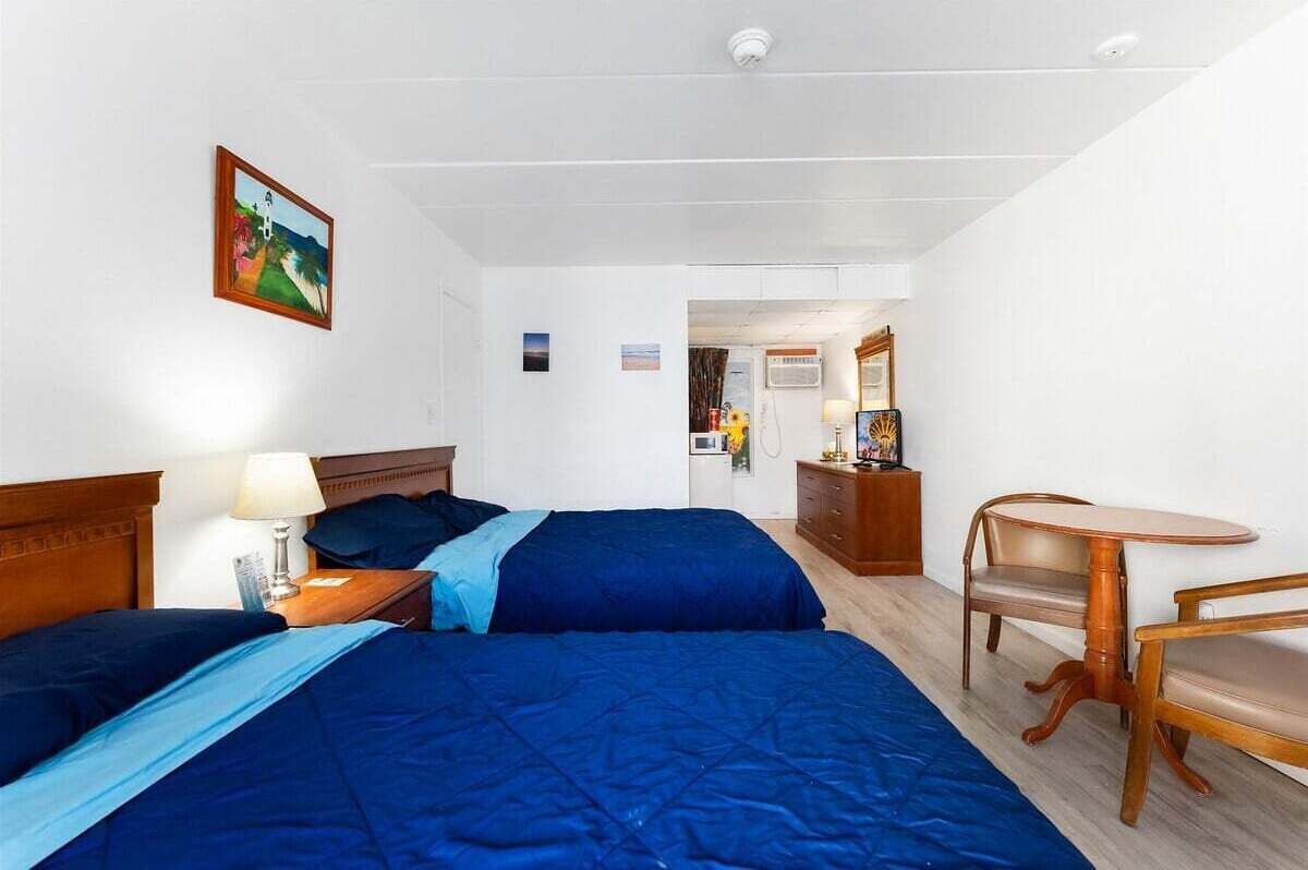 Een hotelkamer met twee bedden, een houten nachtkastje, een tafel met stoelen en een schilderij aan de muur.