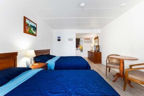 A hotel room with two beds, a wooden nightstand, a table with chairs, and a painting on the wall. - Studio Condo in Prime Location with a Pool (Wildwood)