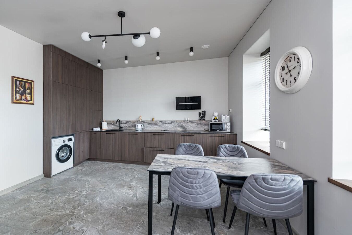 A modern kitchen with a built-in washer, a dining area with a marble table, and a large window with blinds.