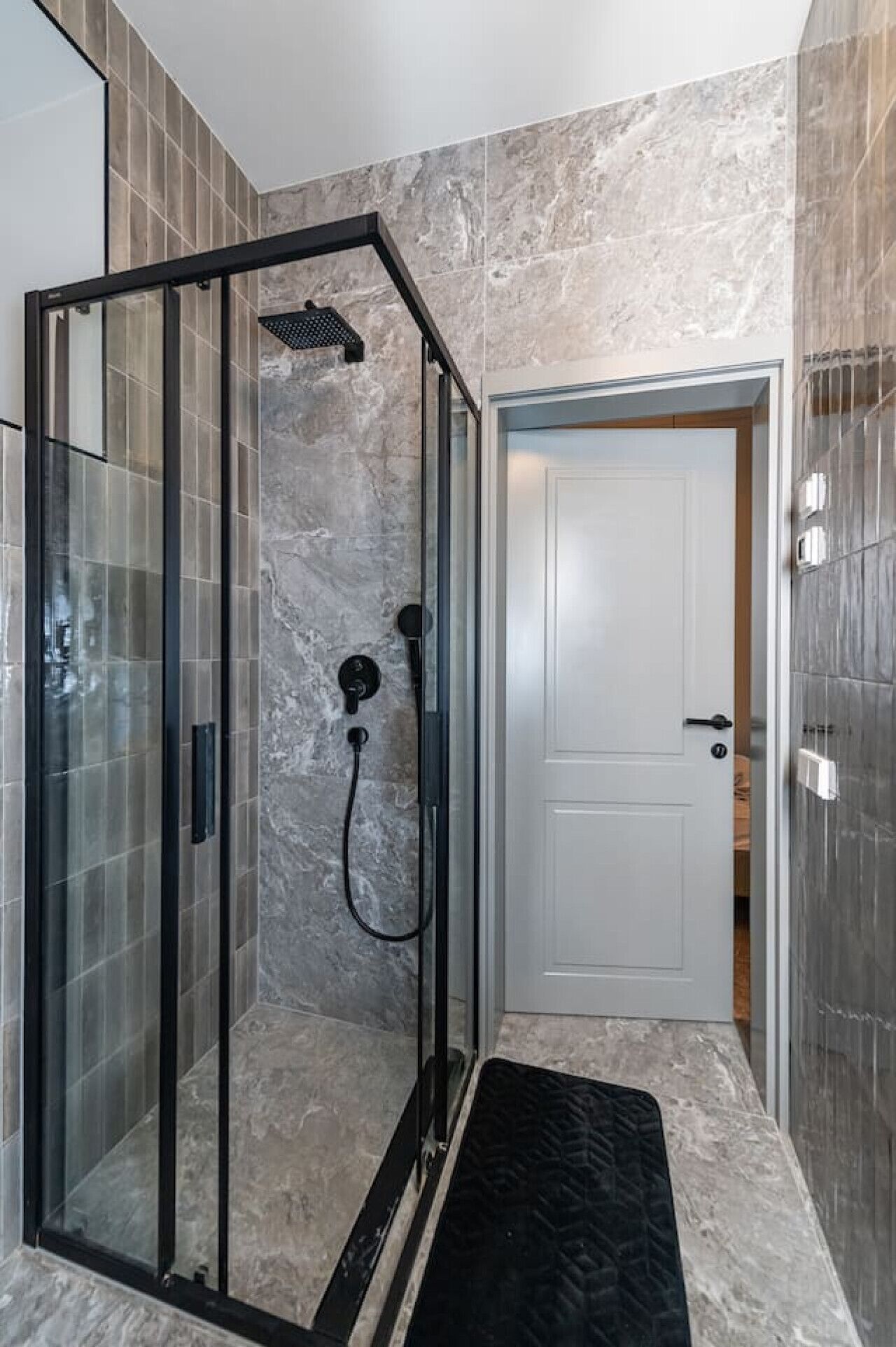 Een moderne badkamer met een douchecabine van glas, marmeren wanden en een witte deur.
