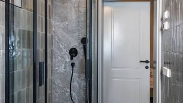 Een moderne badkamer met een douchecabine van glas, marmeren wanden en een witte deur.