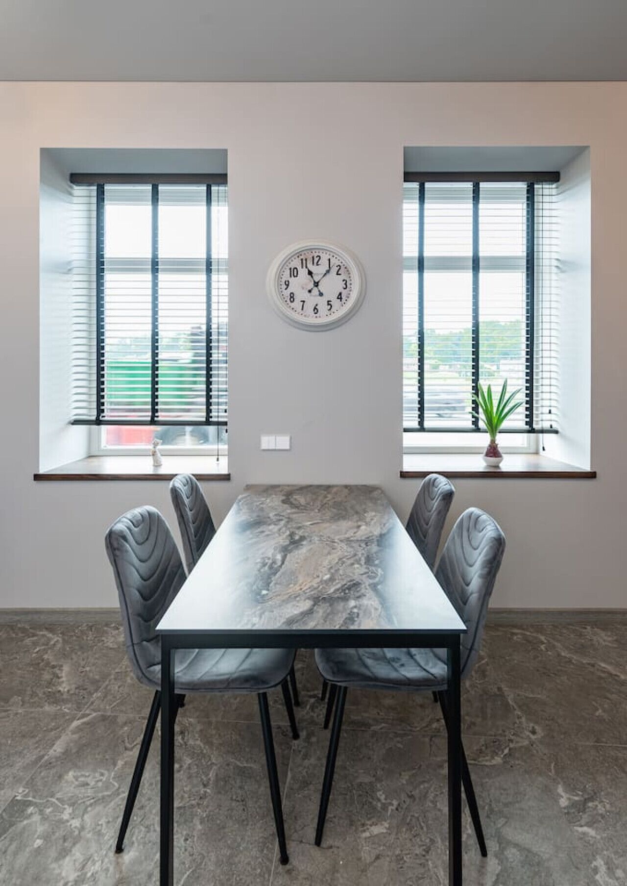 Une salle de conférence avec une table en marbre, quatre chaises, une horloge et deux fenêtres équipées de stores.